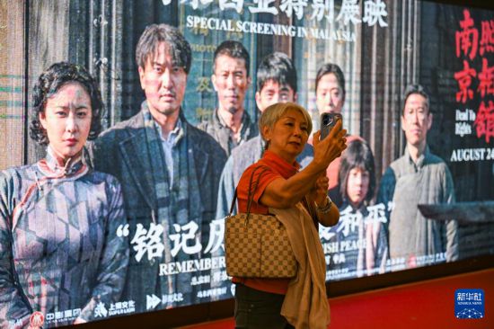 8月24日,在马来西亚吉隆坡,一名观众观影后同《南京照相馆》海报合影留念。新华社记者 程一恒 摄